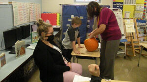 A student watches as Mrs. Haswell scoops out seeds