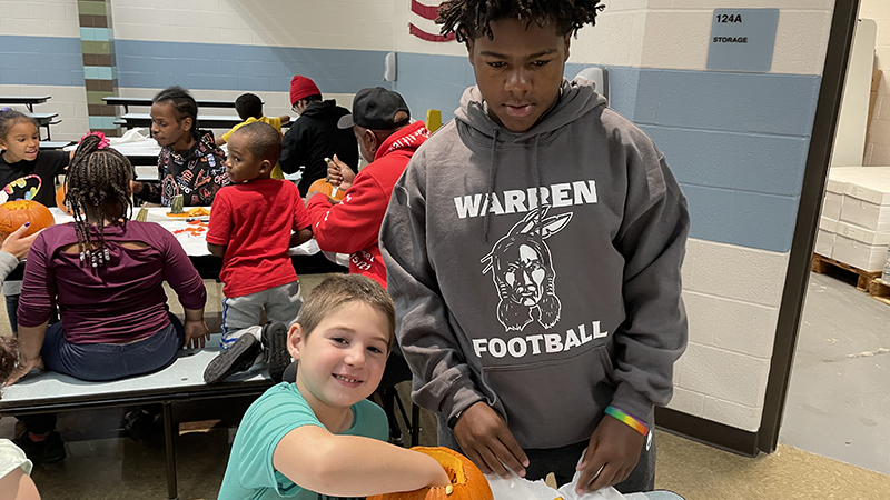 A student council member helps a student with his pumpkin.