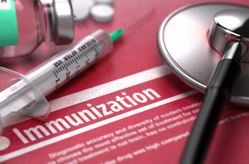 Immunization - Medical Concept on Red Background with Blurred Text and Composition of Pills, Syringe and Stethoscope.